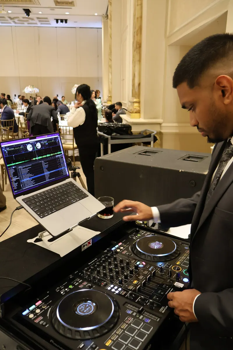 DJ Shadzy mixing at a wedding reception with guests seated in the ballroom behind him